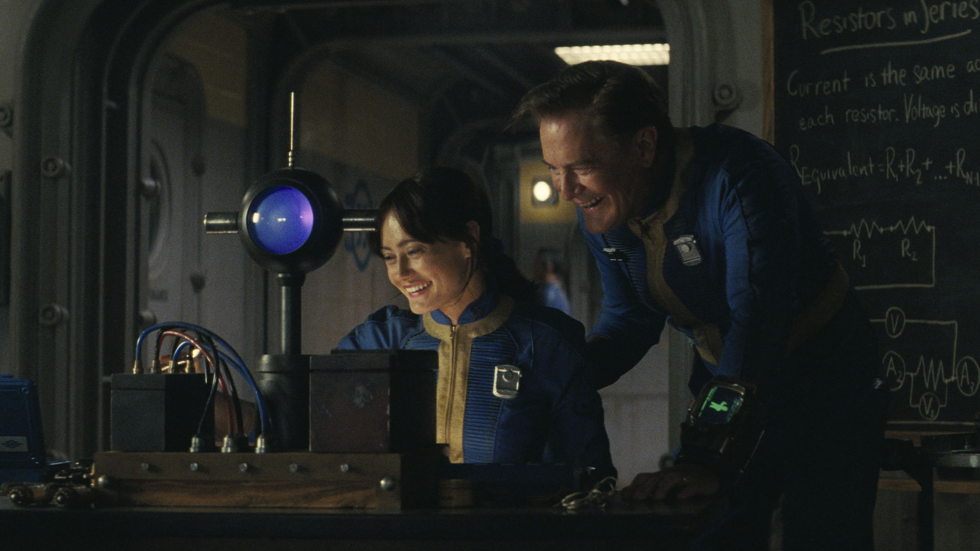 لوسی و هنک در حالی که در برنامه تلویزیونی Fallout به صفحه کامپیوتر نگاه می کنند، شوخی به اشتراک می گذارند