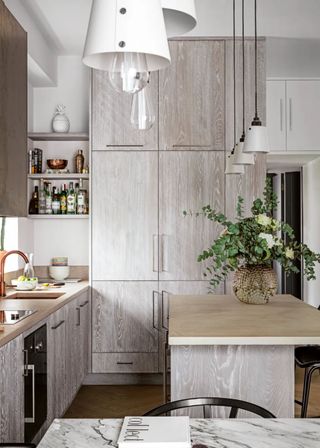 Floor-to-ceiling cabinets add dimension to the kitchen space. A large island is seen with pendants above and a pot with flowers.