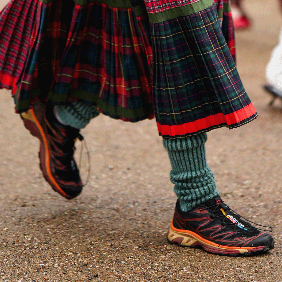 A guest wears a yellow turtleneck pullover, a navy blue with yellow embroidered pattern zipper sport sweater, a pale blue matte leather crossbody bag from Telfar, a red / green / black checkered print pattern midi skirt, a black umbrella, green ribbed wool high socks, black and orange sneakers from Salomon, outside OperaSport, during the Copenhagen Fashion Week Spring/Summer 2024 on August 09, 2023 in Copenhagen, Denmark. Photo by Edward Berthelot/Getty Images.