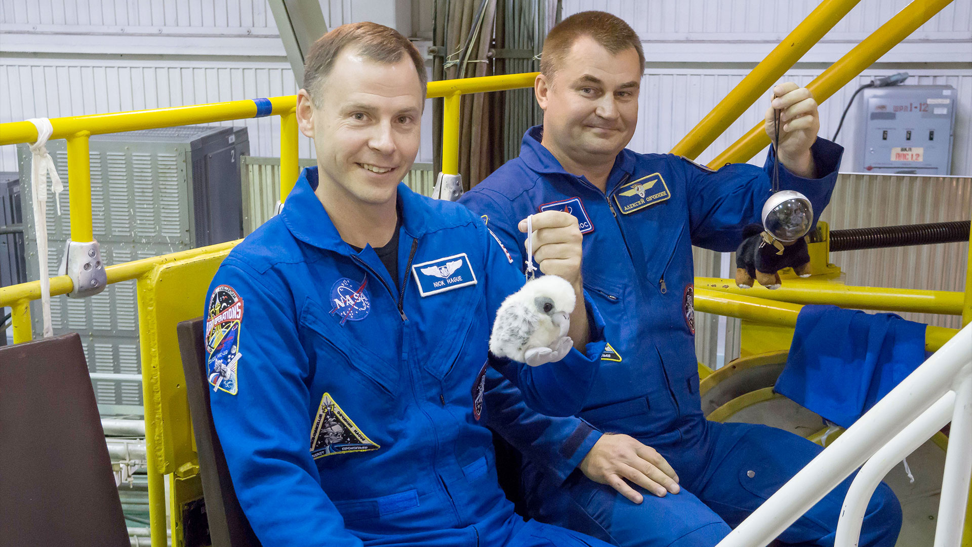 NASA astronaut Nick Hague and Roscosmos cosmonaut Alexey Ovchinin hold up their Soyuz MS-10 zero-g indicators, including "Aurora," a baby falcon plush toy that Hague flew again on SpaceX's Crew-9 launch on Saturday, Sept. 28, 2024.