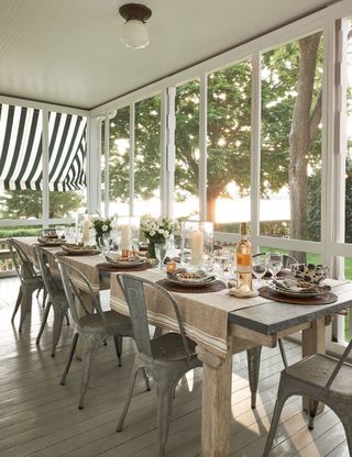 dining table set for lunch on covered porch area with striped awnings and metal tolix chairs