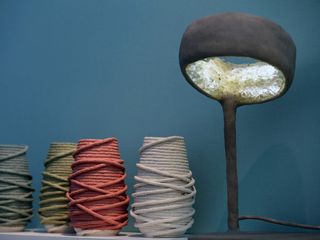 View of 'Lightweight Porcelain' by Djim Berger and the 'Luciferase' lamp by Nacho Carbonell - four colourful structures that resemble yearn and a dark grey and white sculpted table lamp against a dark blue background