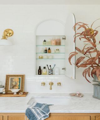 Wall-mounted bathroom cabinet with shelves lined with beauty products, positioned above marble bathroom countertop