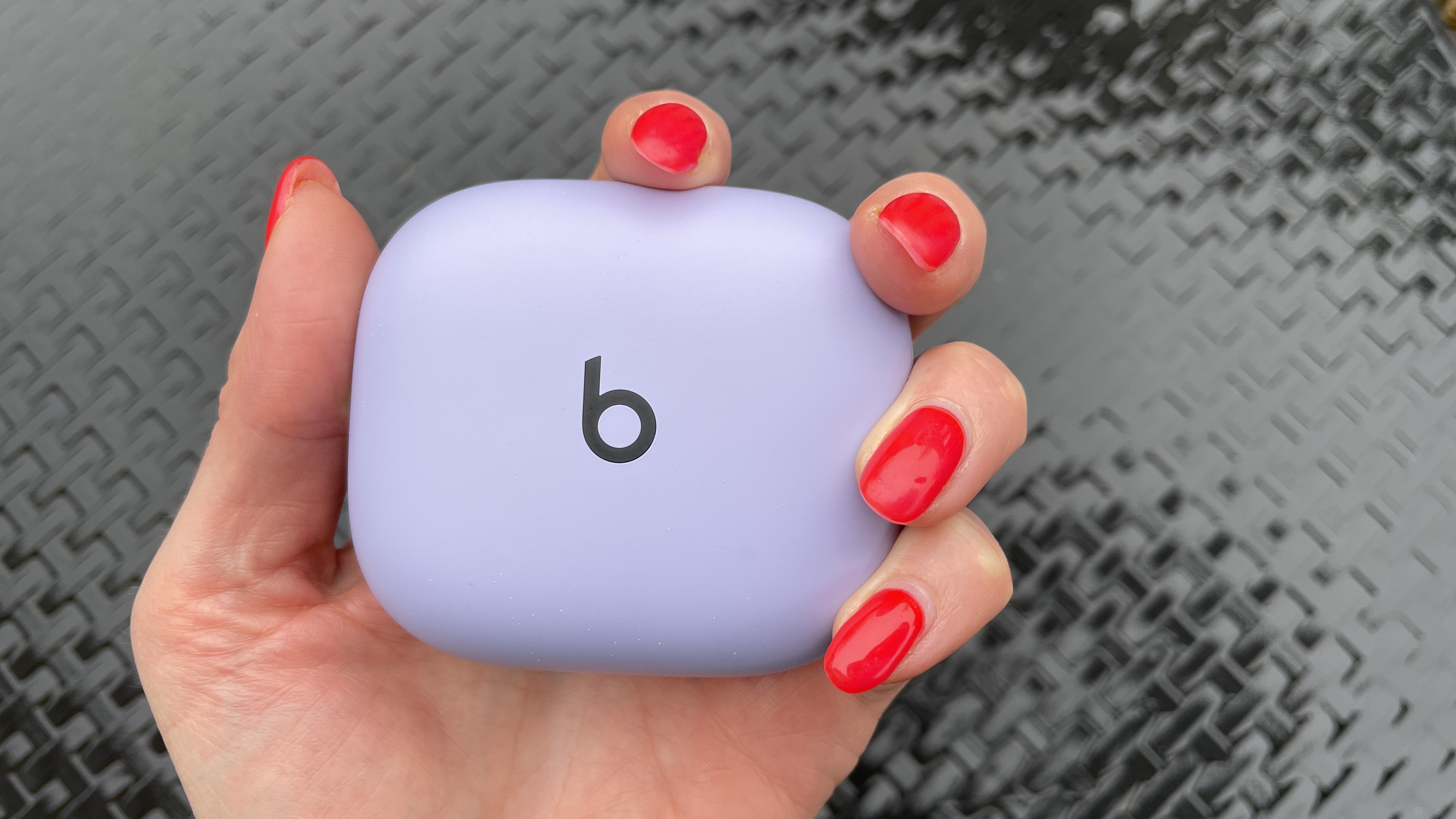 A hand holding the Beats Powerbeats Pro 2 case, outside on a rainy day