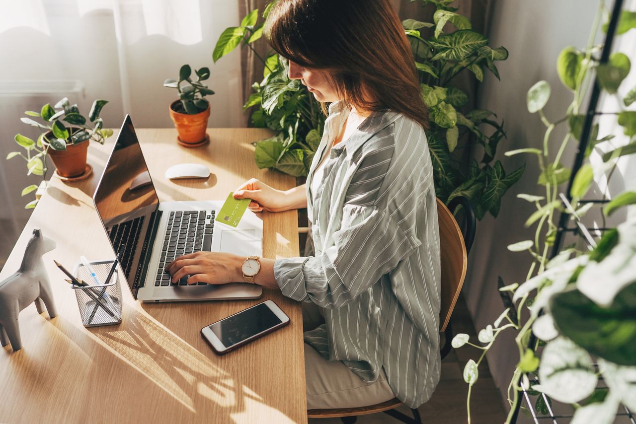 Young woman holding credit card and using laptop computer. Businesswoman working at home. Online shopping, e-commerce, internet banking, spending money, working from home concept - stock photo