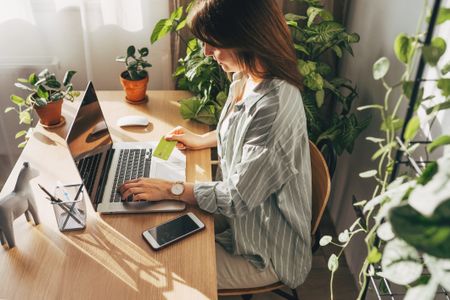 Young woman holding credit card and using laptop computer. Businesswoman working at home. Online shopping, e-commerce, internet banking, spending money, working from home concept - stock photo