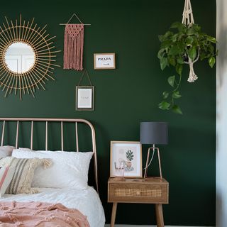 green bedroom with copper bed frame wood bedside table grey table lamp macrame plant hanger rattan mirror white bedding pink throw