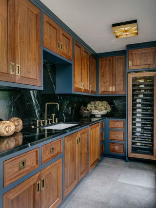 butlers pantry with dark wood cabinets black backsplash wine fridge and pale floor tiles