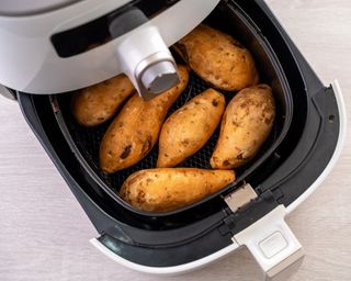 Six sweet potatoes in white air fryer basket being cooked