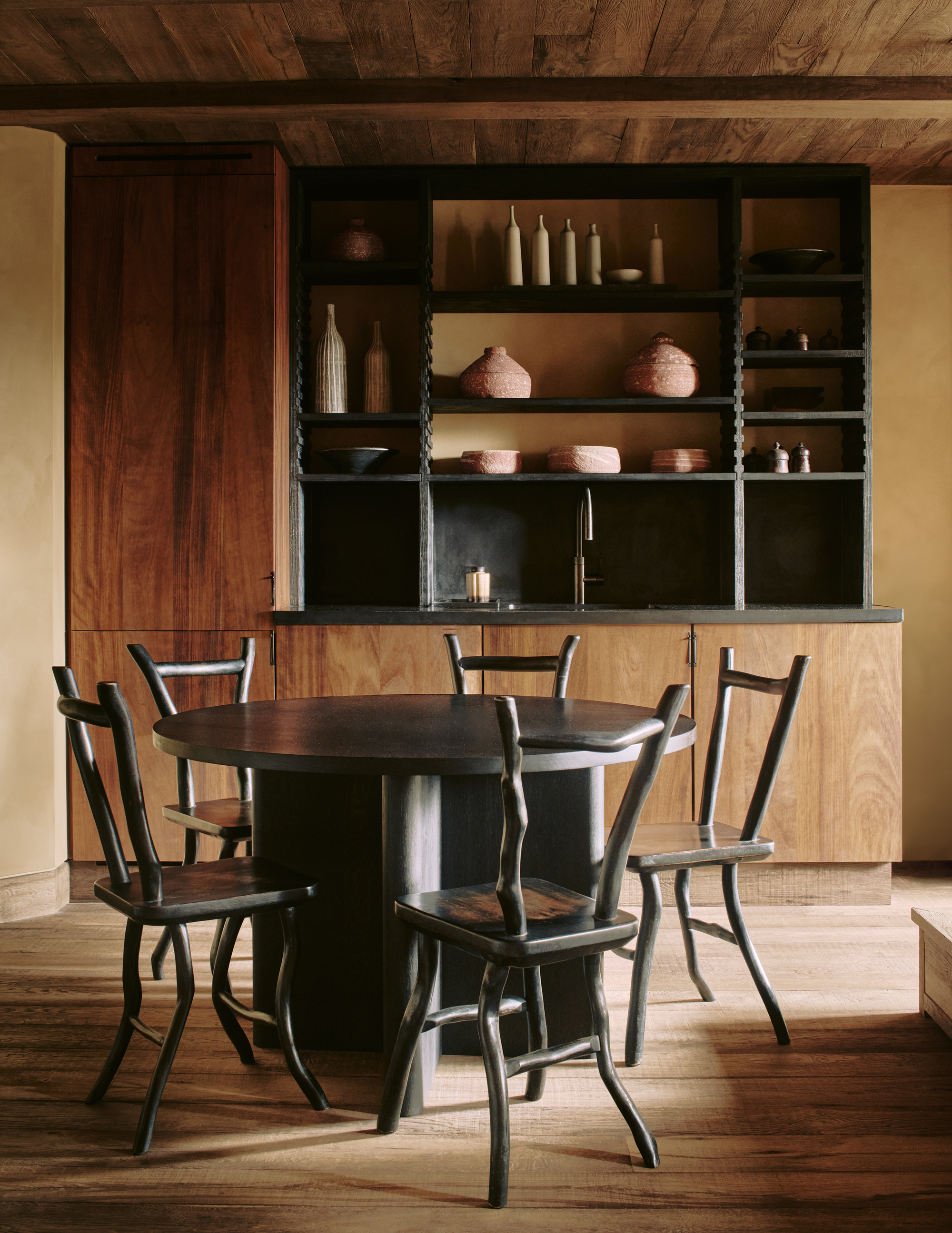 Image of a room with wooden cabinetry, wooden floors, and a wooden ceiling. There is a black circular table with matching chairs around it.
