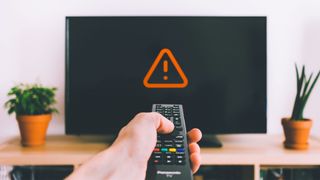A hand holds a remote pointed at a blank TV with a warning triangle on it 