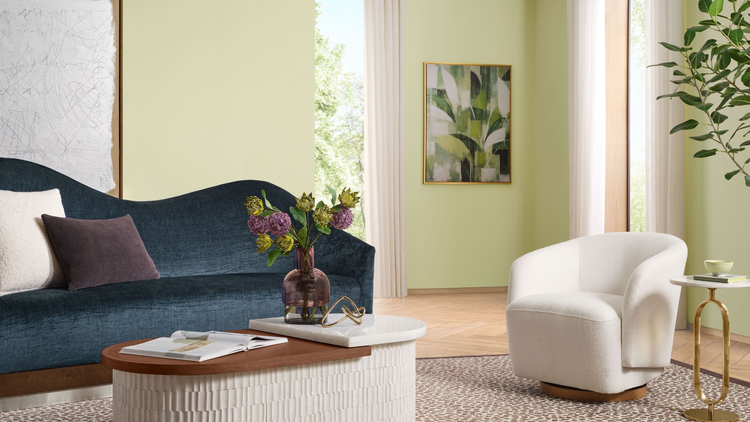 Living room painted in Sherwin-Williams Celery, with wooden floors, a boucle cream armchair, a velvet navy blue curved sofa, a low wooden coffee table and a large olive tree in the corner.