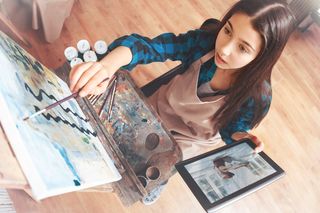 Female student working on painting holding tablet computer