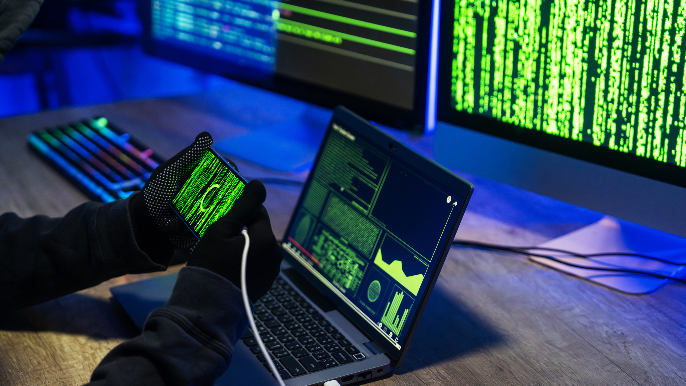 A scene of a hacker engaging in cybersecurity breaches using advanced technology and devices in a dimly lit environment.