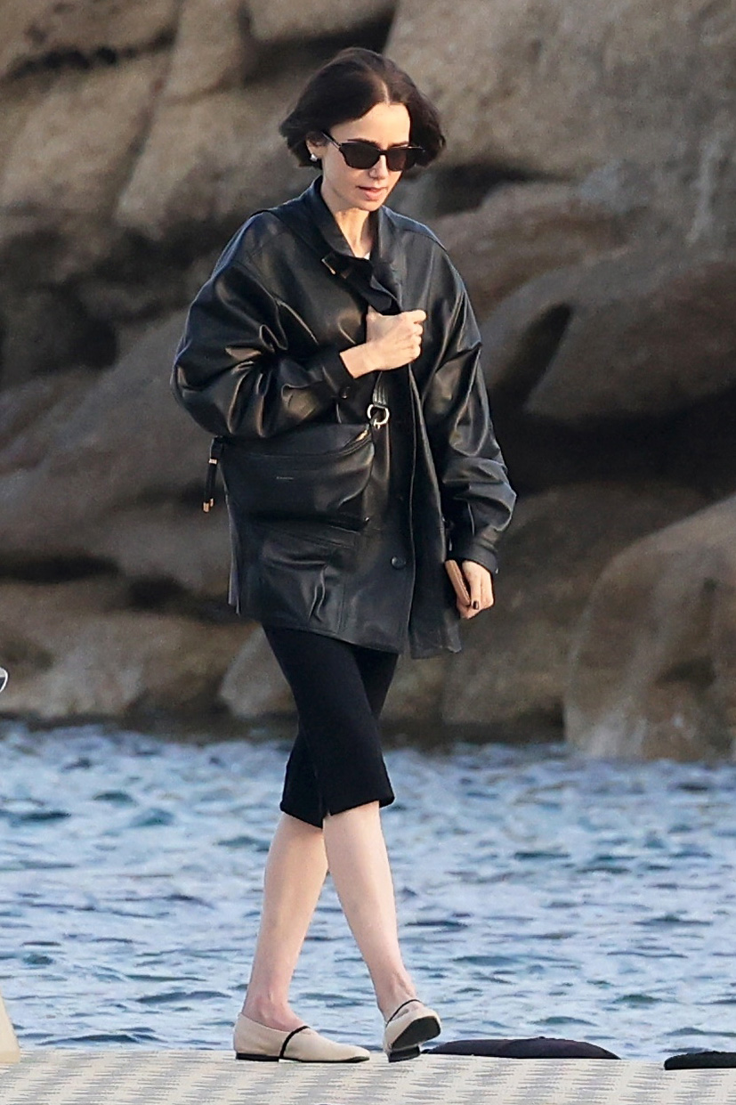 Lilly Collins wearing a black leather jacket, capri pants, and two-tone cream-and-black ballet flats in Mykonos