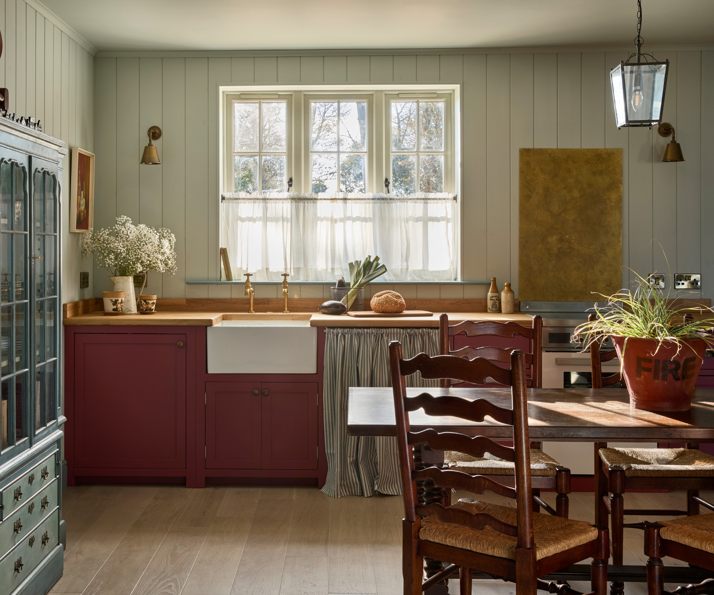 A coastal cottage kitchen with light blue paneled walls, wood counterops and burgundy cabinets