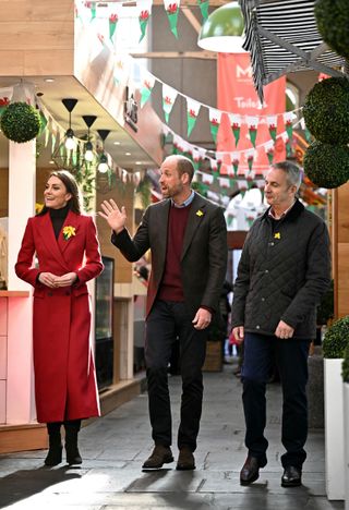 Kate Middleton wearing a red coat walking next to Prince William on a street with Welsh flags