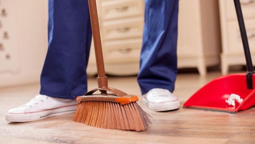 Man sweeping floor with brown mop and red dustpan