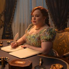 A woman (Nicola Coughlan as Penelope Bridgerton) writes with a feather quill at a Regency-era drawing table, in episode 405 of Bridgerton.