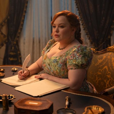A woman (Nicola Coughlan as Penelope Bridgerton) writes with a feather quill at a Regency-era drawing table, in episode 405 of Bridgerton.