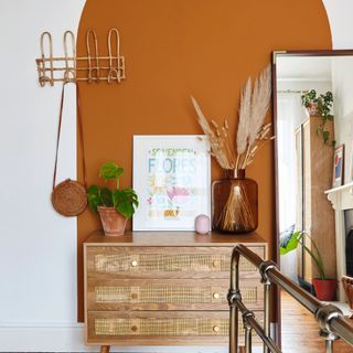 Bedroom with terracotta, rattan, and wood colour scheme with terracotta painted arch on feature wall