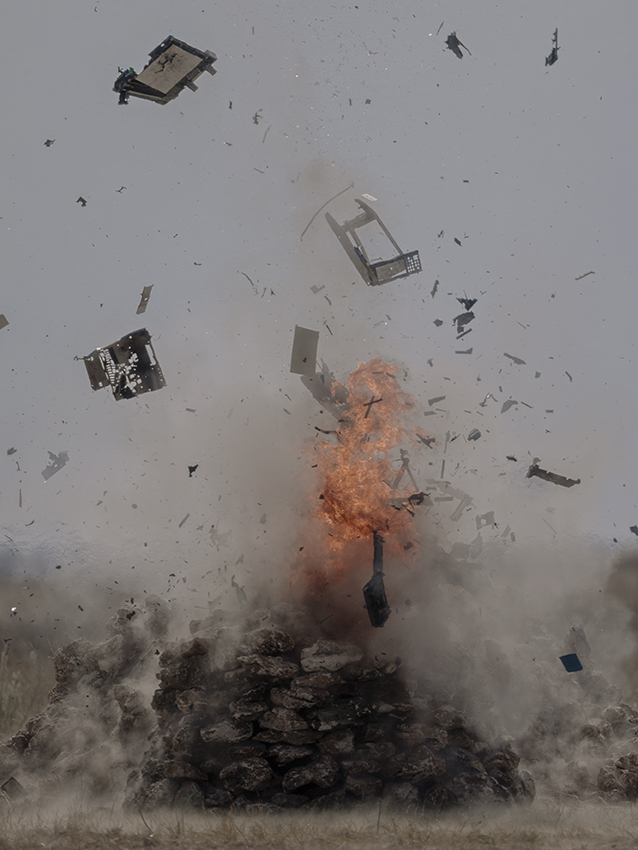 Computer parts fly through the air from a fiery explosion on a pile of rocks