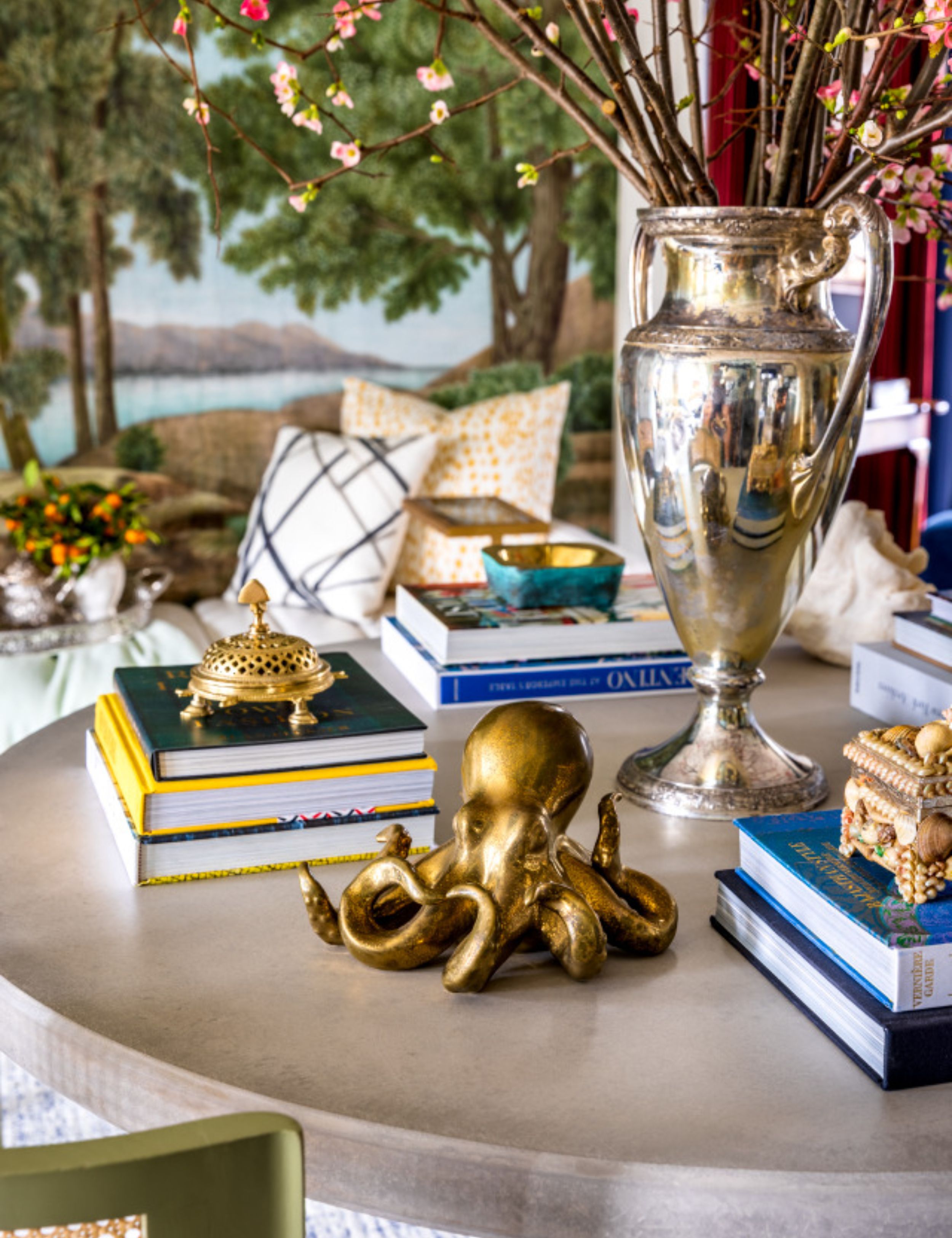 Collected coffee table decor, including an antique pewter urn vase, several book stacks, and a brass octopus sculpture