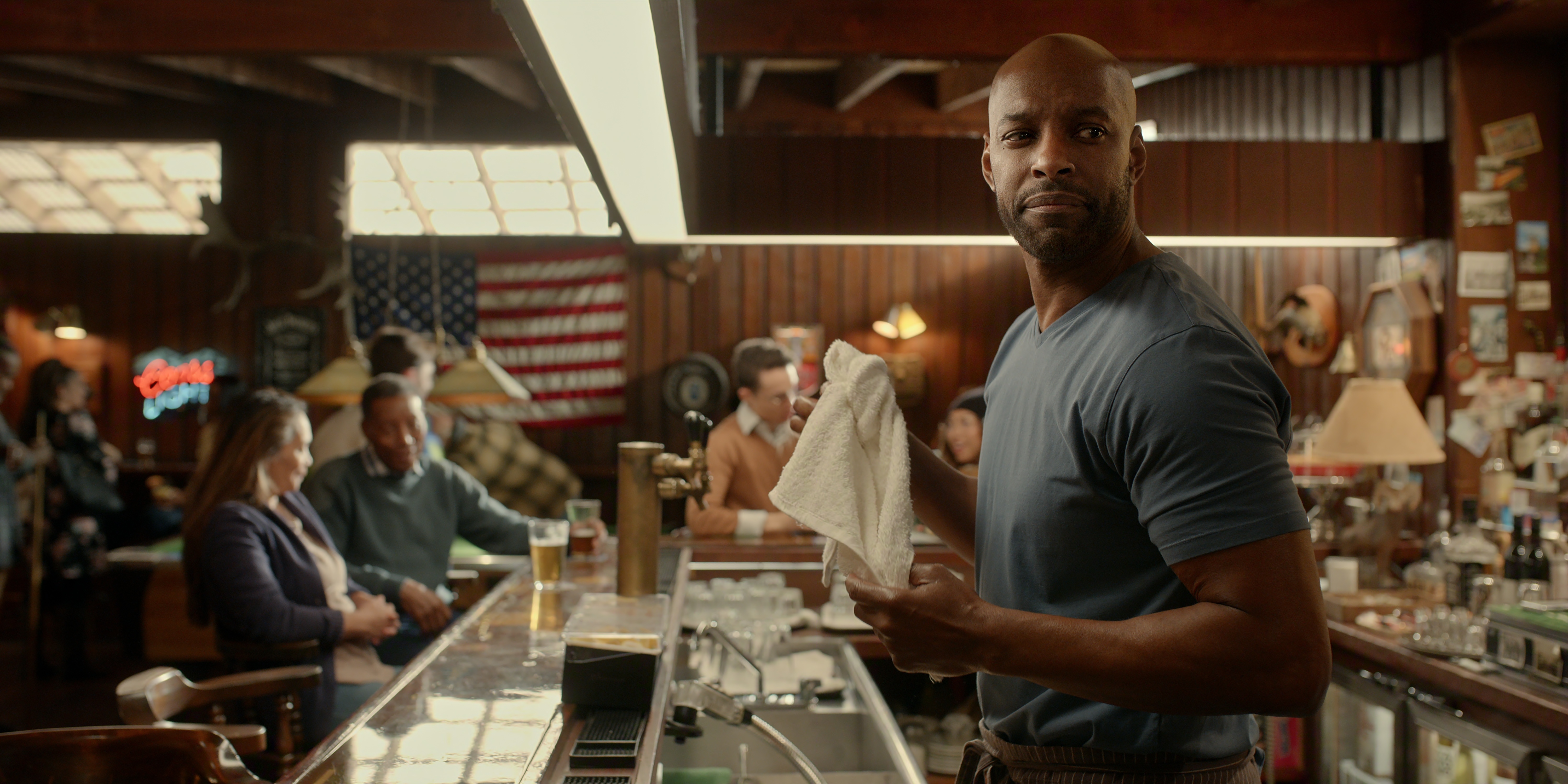 Colin Lawrence as John 'Preacher' Middleton in Episode #703 of Virgin River Season 7 standing behind a busy bar