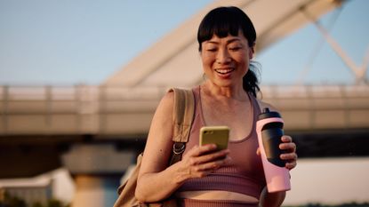Woman looking at phone after workout holding water bottle