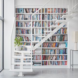 room with white stair case and book shelves and white wall and books