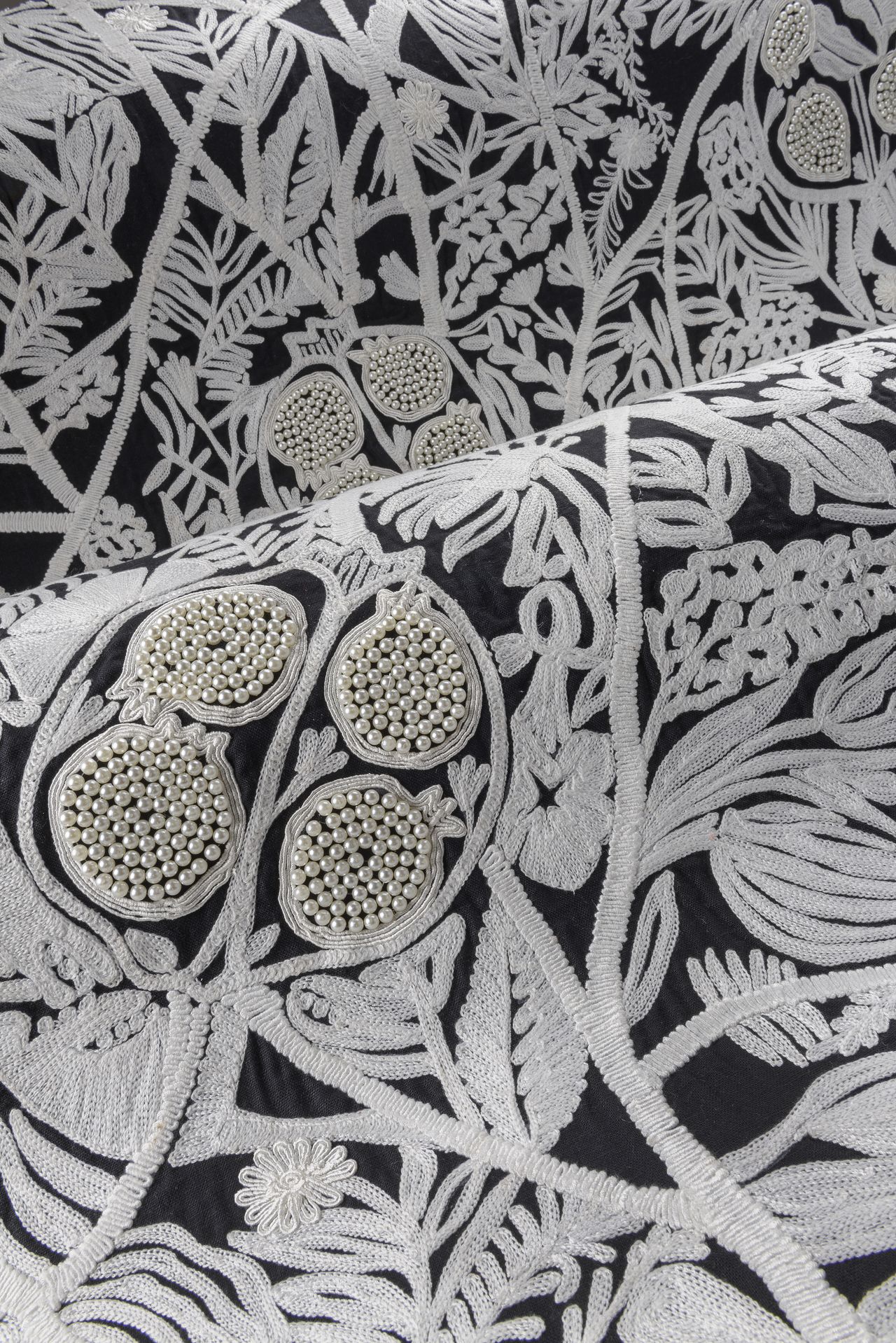 Close-up image of a black fabric wallcovering/wallpaper. It is embroidered with white leaves and foliage designs. There is pearl beading sewn into the fabric.