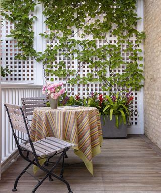 A decking scheme with wooden bistro set, striped tablecloth and white lattice wall paneling