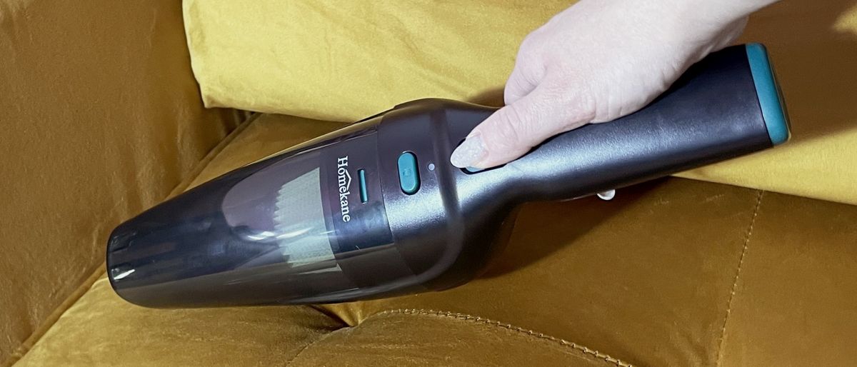 A woman is vacuuming a mustard colored sofa with the Homekane Handheld Vacuum.