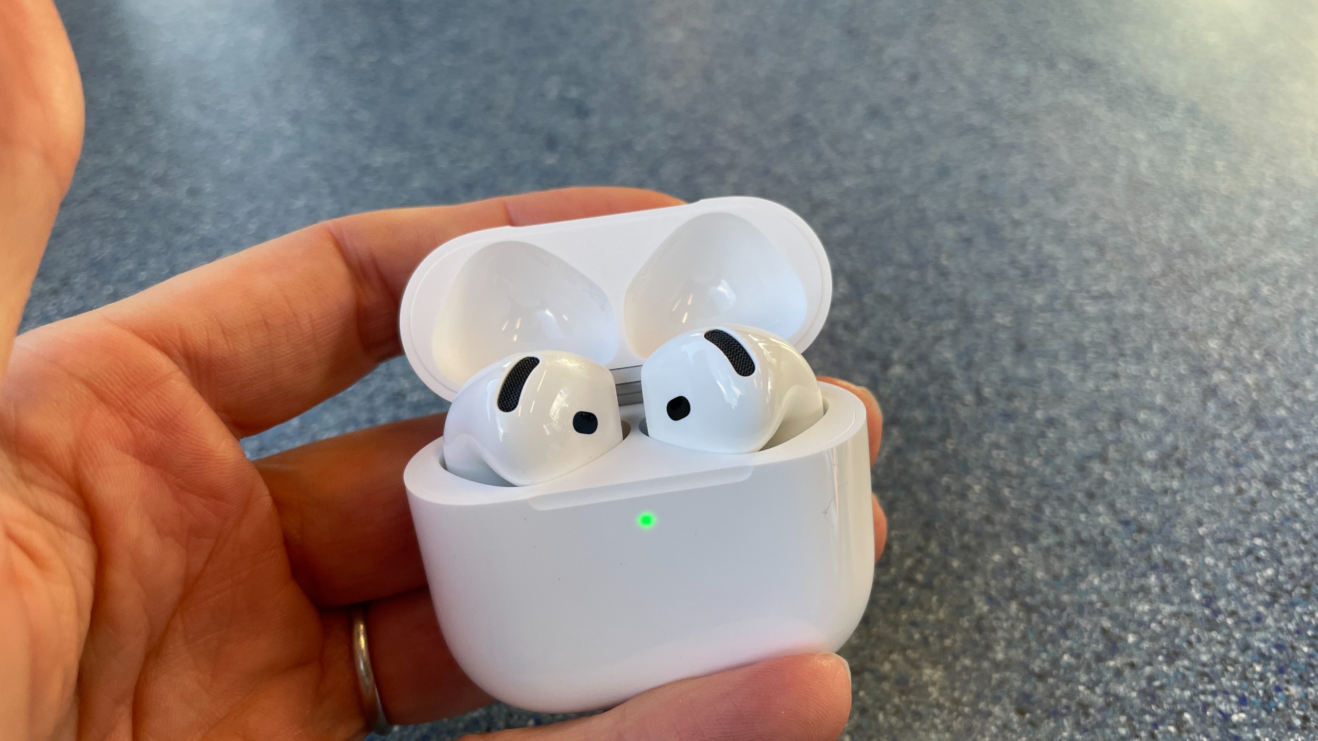 Apple AirPods 5 with Wireless Charging, on a blue table and held in a hand