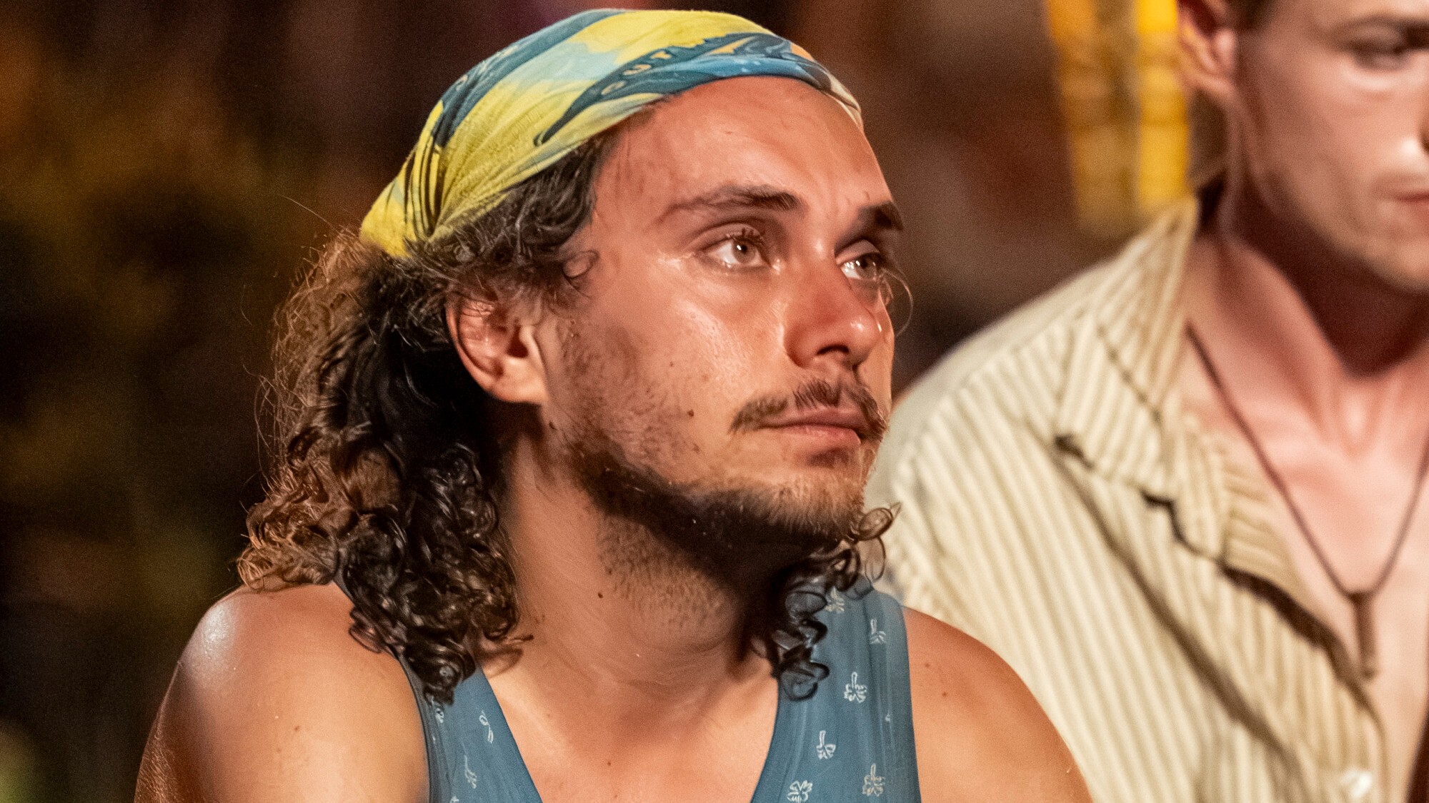 Kilby listening at the latest tribal council. He's wearing his Toka buff and has a serious face. 