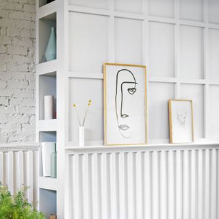 White wall with abstract paintings and minimalistic accessories on the shelves