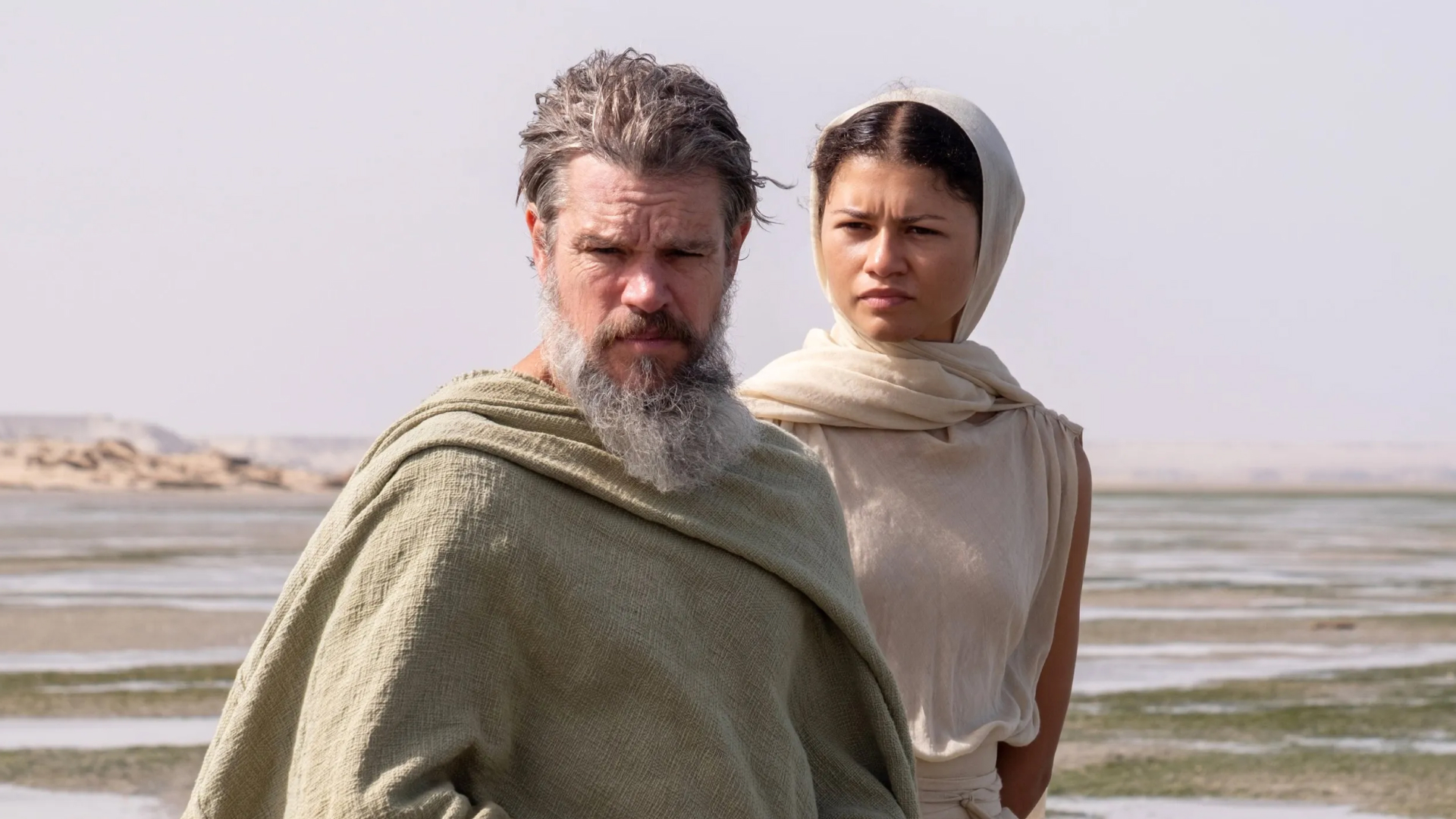 matt damon as odysseus and zendaya as athena standing on a beach in the odyssey