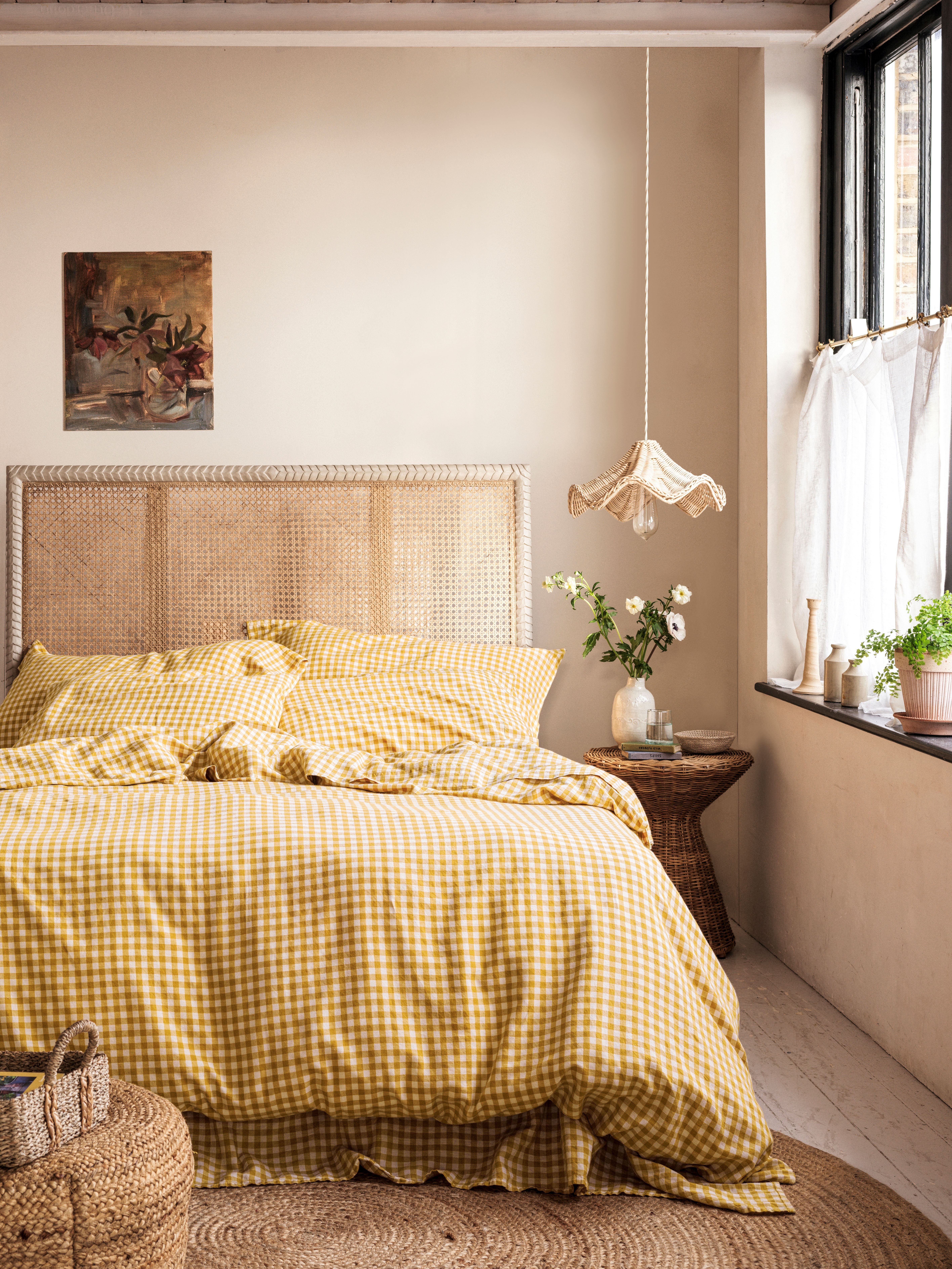 A yellow gingham printed duvet on a light wicker bed with a wicker bedside table with white flowers on it