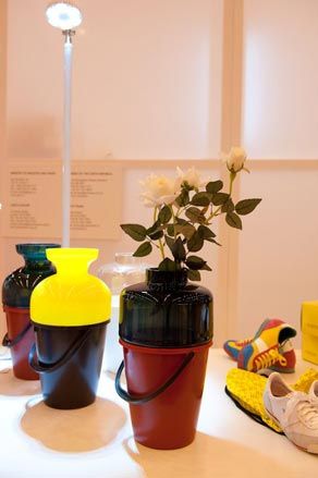 Three vases in colour block design photographed on a white surface next to pair of trainers