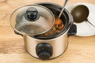 A slow cooker with cooked food inside on a kitchen worksurface