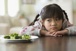 Close up of a little girl staring at a plate of broccoli