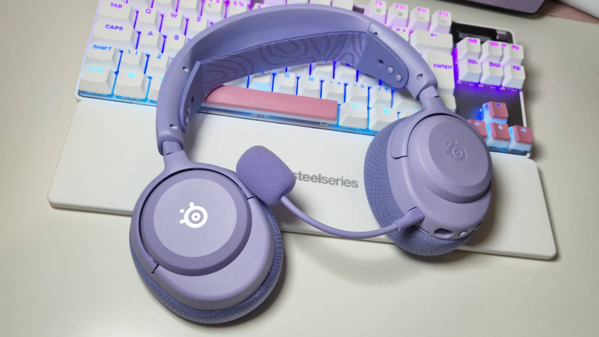 Photos of the SteelSeries Arctis Nova 3 Wireless gaming headset in Lavender, taken by writer Rosalie Newcombe, on a white desk.