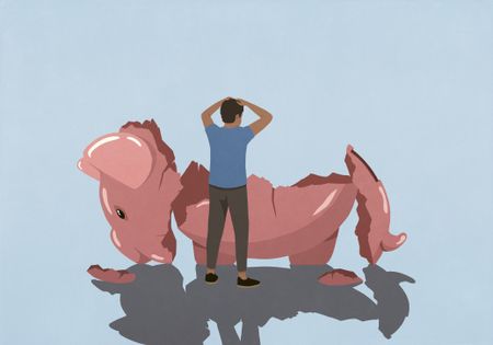 A stressed man looking at broken piggy bank 
