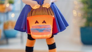 Child carrying pumpkin bucket for trick or treating wearing a face mask