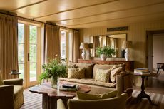 a living room painted in a golden paint color with beadboard walls, curtains on window and a ochre couch