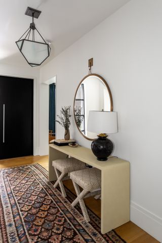 Entryway with console table topped with lamp with wall mirror.