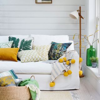 white small living room with cream sofa and pompom throw with yellow and green cushions