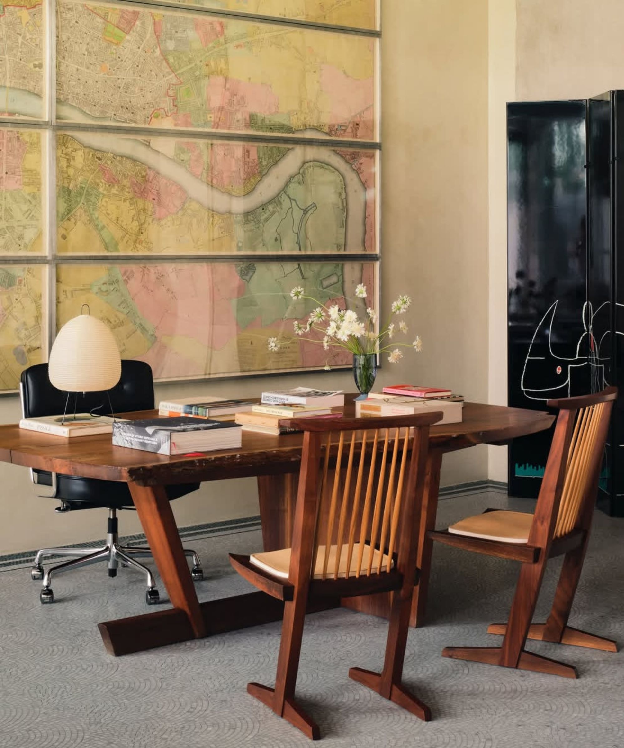 Large modern study with large wooden table and chairs, black and metal desk chair, large map artwork behind desk, black screen to left