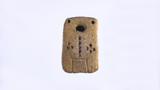 Anthropomorphic light brown clay tablet shaped like a domino with circular depressions scattered across it