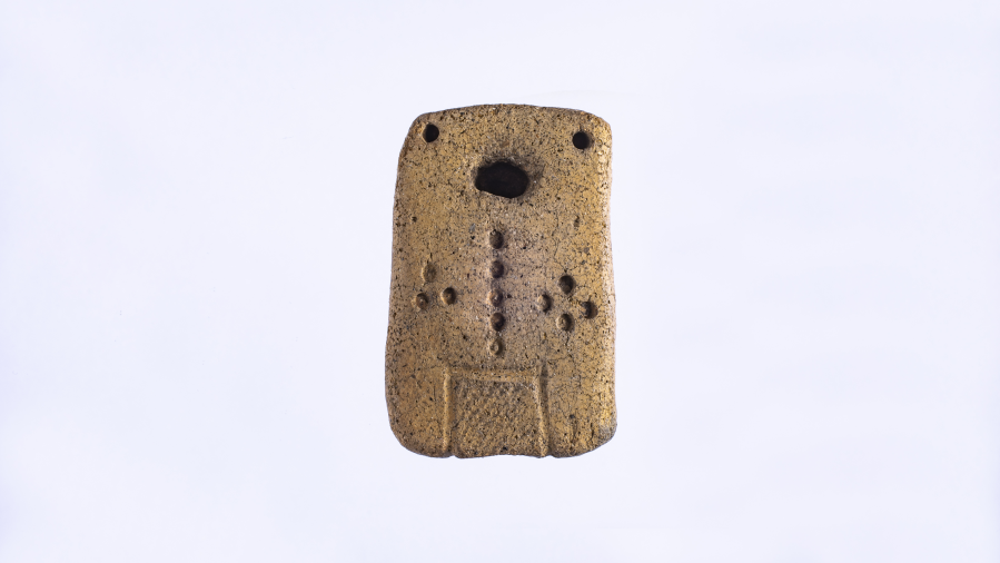 Anthropomorphic light brown clay tablet shaped like a domino with circular depressions scattered across it